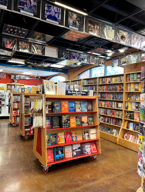 A cozy bookstore interior featuring shelves of books and a display stand in the center.